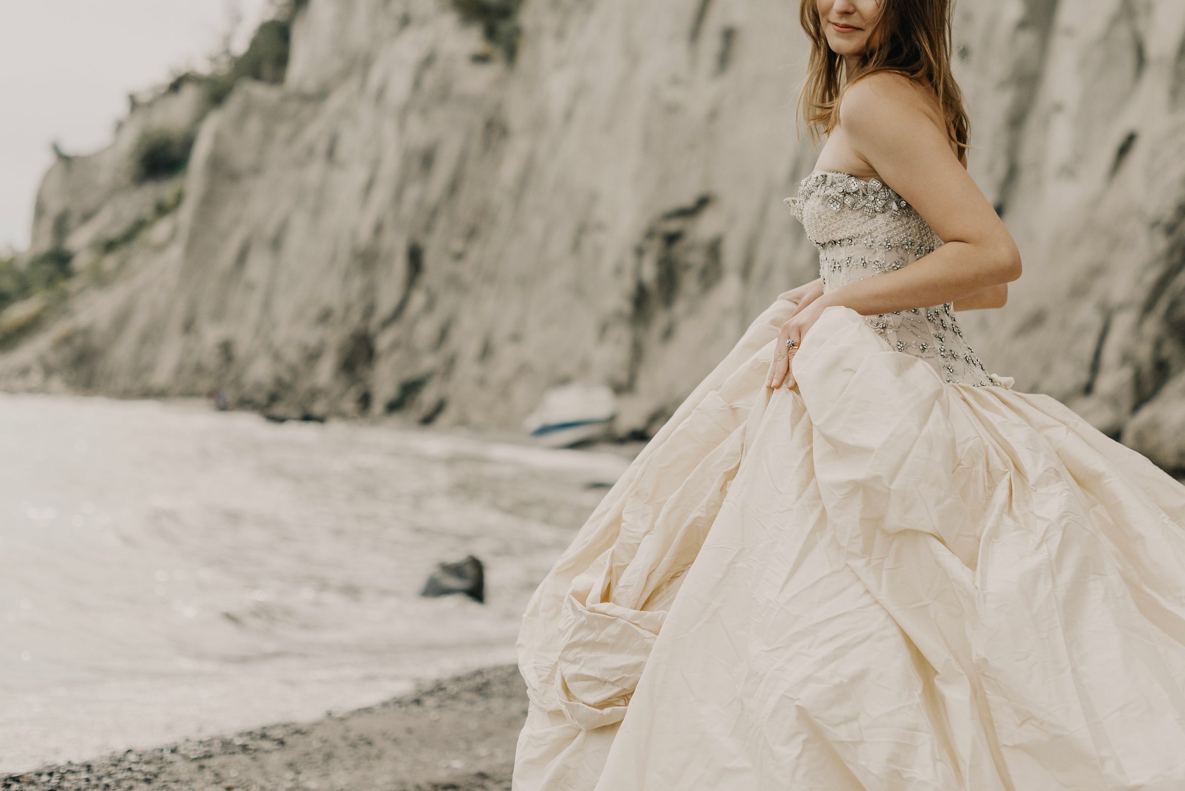 bride posing in designer wedding dress with beaded corset and large puffy skirt on the sands of a beach